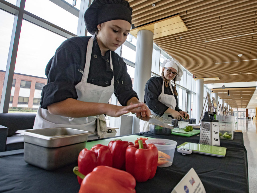 Marissa Halbig, left, and Madison Halsey, center, work on their pineapple chicken stir-fry dish for the HUNCH Culinary Challenge. Credit: NASA